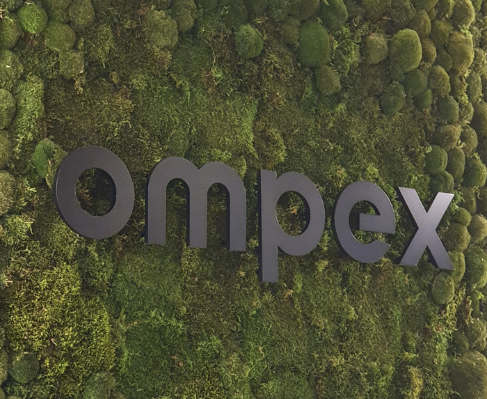 Ompex - Das schwarze Firmenlogo wirkt elegant auf dem Moos.
